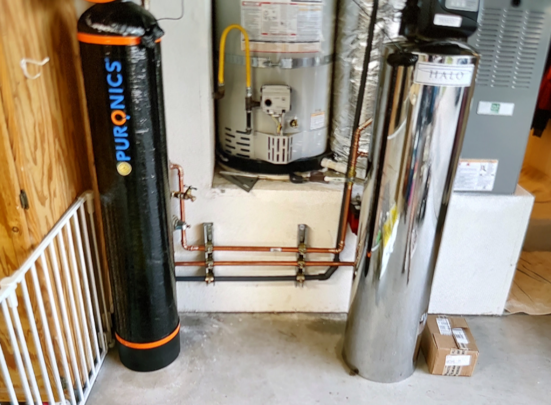 Water softening and treatment tanks installed in a garage alongside copper supply piping.